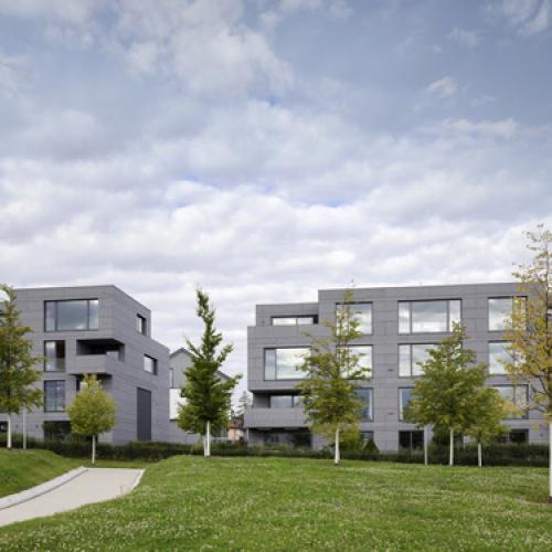 Die Fassaden sind einheitlich mit Faserzementtafeln bekleidet. Die homogene, alle Details umfassende Hülle verstärkt das Zusammenspiel der beiden Wohnhäuser einer Baugruppe und verleiht ihnen eine starke eigene Identität. Foto: David Franck, Ostfildern