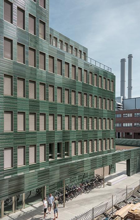 Die unregelmäßig abgetreppte Kubatur des Holz-Hybrid-Baus wird durch das schmale Grundstück und die Abstandsflächen bestimmt. Während die Stirnseiten des Büro- und Verwaltungsgebäudes großflächig verglast sind wurden die Längsseiten mit grün glasierten keramischen Fassadenplatten mit einer feinen horizontalen Reliefstruktur bekleidet. Die individuelle Sonderanfertigung aus dem Hause Moeding Keramikfassaden GmbH entstand in enger Abstimmung mit den Architekten. Foto: Anke Müllerklein